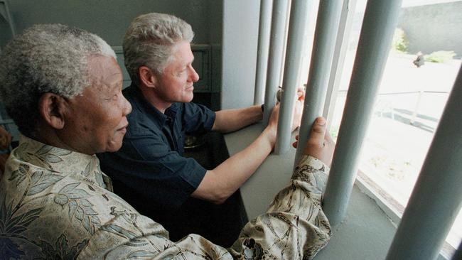 Former South African President Nelson Mandela and then US President Bill Clinton peer out from Section B, prison cell No. 5, on Robben Island, South Africa in 1998. Picture: AP.