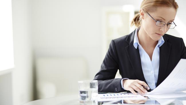 Young businesswoman sitting at workplace and reading paper in office