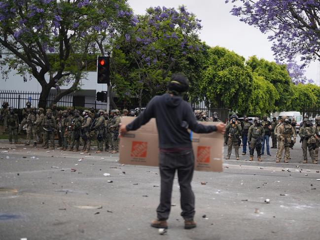 A protester holds a sign as Border Patrol personnel in riot gear and gas masks stand guard outside an industrial park in the Paramount section of Los Angeles. Picture: AP