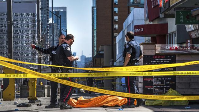 Police officers stand by a body covered on the footpath in Toronto after a van crashed into a crowd of pedestrians. Picture: Aaron Vincent Elkaim/The Canadian Press via AP.