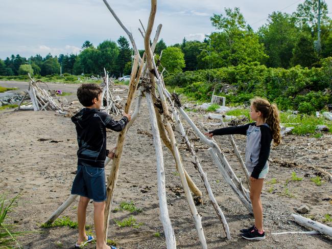 Boy and girl making a teepee with tree trunk found on the beach of the St. Lawrence river in Gaspesie (Les Mechins) during summer day vacations.