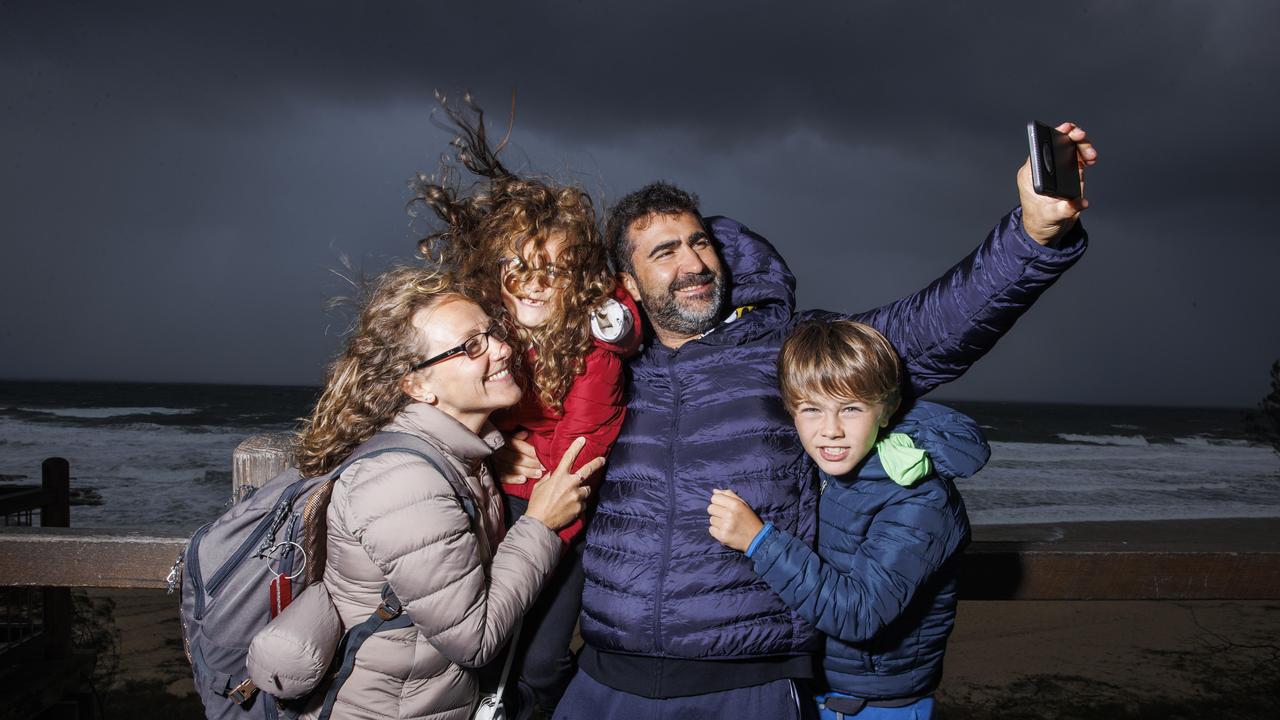 Flavie and Emeric Boussely from France attempt to take a selfie in gale-force conditions with children Siloe, 6, and Timote, 9, at Buddina while on holiday on the Sunshine Coast. Picture Lachie Millard