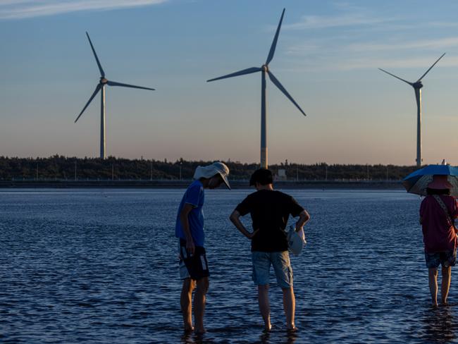 TAICHUNG, TAIWAN - AUGUST 22: Wind turbines stand behind visitors at Gaomei wetland during sunset on August 22, 2024 in Taichung, Taiwan. Taiwan, a leader in utilising natural resources for power, is rapidly expanding its wind power generation, particularly through offshore projects, to meet its renewable energy targets. By 2025, the government aims for wind energy to contribute 3 GW to its goal of 10 GW from renewable sources, leveraging the island's strong wind resources and favorable conditions for offshore developments. (Photo by Annabelle Chih/Getty Images)