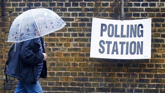 A man shelters from the rain as he arrives at a polling station in London. Picture: AFP
