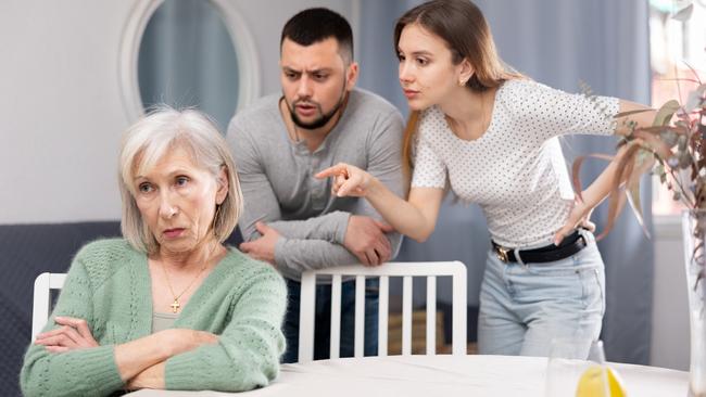 Old woman ignoring her daughter and son-in-law standing behind and arguing with her at home.; generation argument greed generic