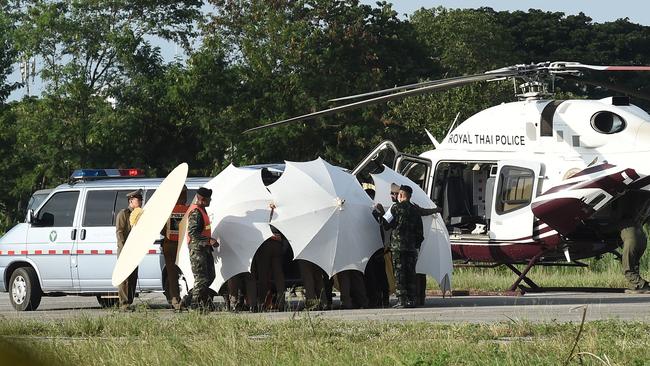 Police and military personnel use umbrellas to cover around a stretcher near a helicopter and an ambulance at a military airport in Chiang Rai. Picture: AFP