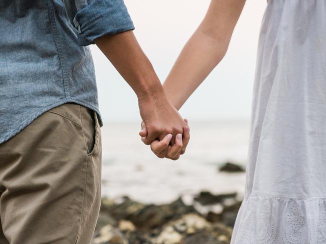 Caucasian young woman with her Japanese boyfriend holding hands at the beach.