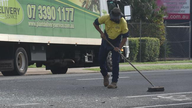 A workman helps sweep glass off the road.