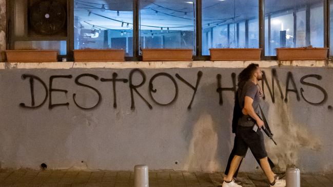 A person carrying a gun, with his arm around a woman walks past a spray painted sign that reads "Destroy Hamas" on October 30, 2023 in Tel Aviv, Israel. Picture: Alexi J. Rosenfeld/Getty Images