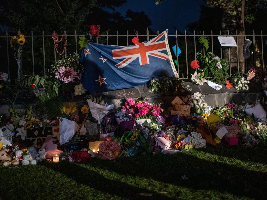 Shadows are cast onto a New Zealand flag hung among flowers and tributes on the wall of the Botanic Gardens in Christchurch. Picture: Getty Images