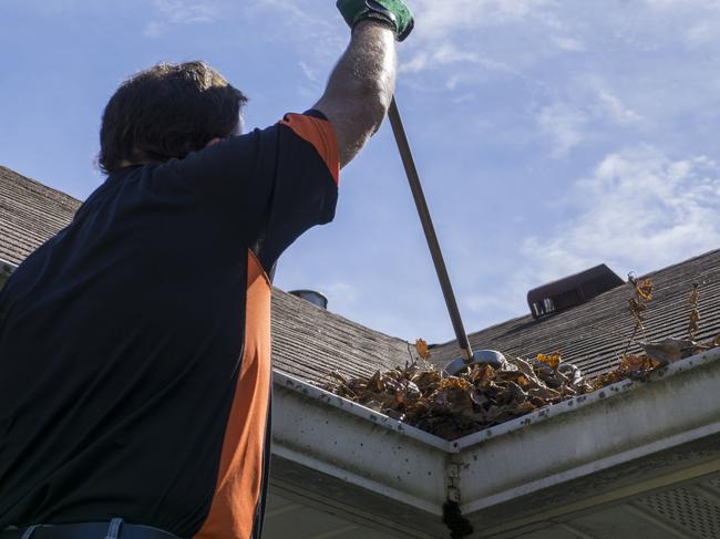 f03trade. Worker sweeping leaves and sticks from a valley of a roof.