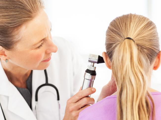 Female doctor examining girl's ear with otoscope in hospital. Horizontal shot.