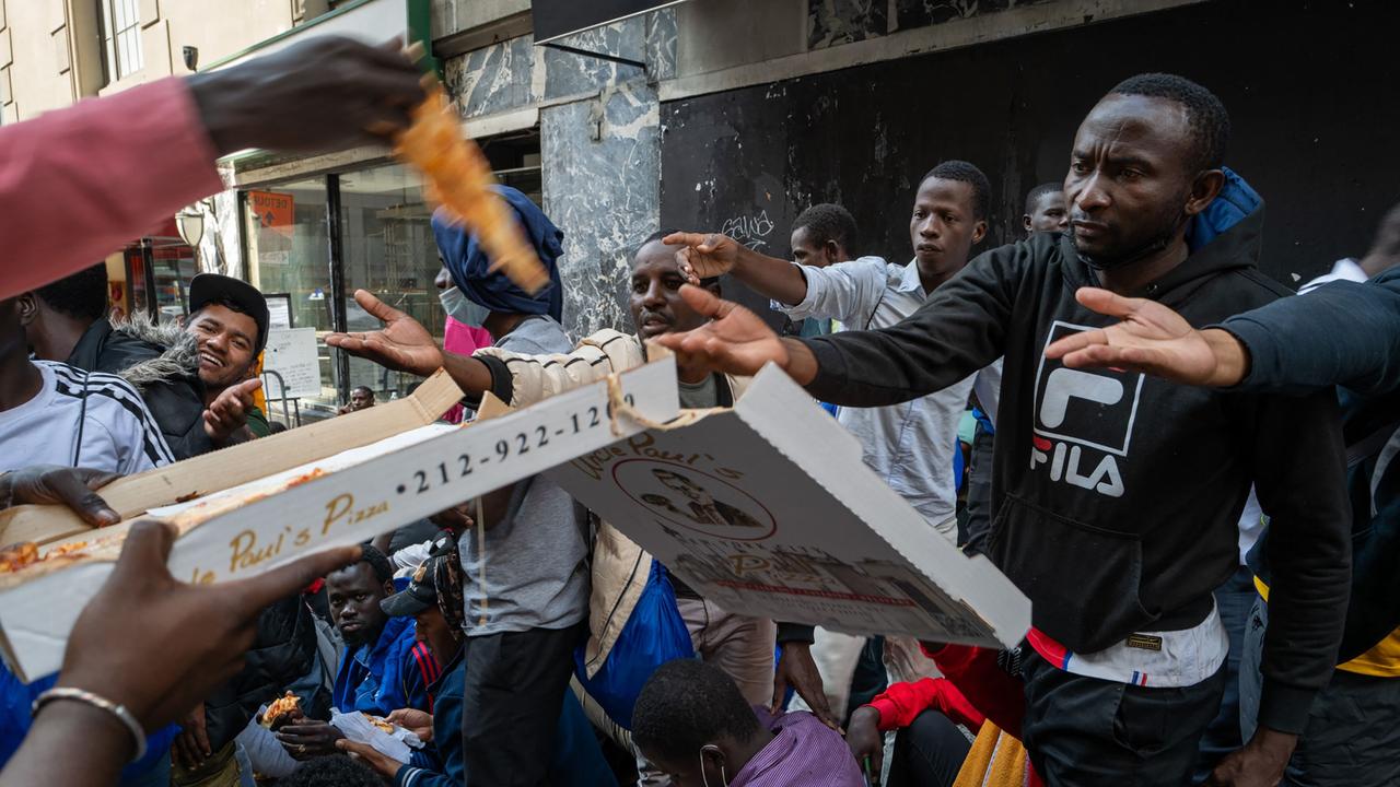 Migrants hold their hand out for the final slice of pizza (Photo by SPENCER PLATT / GETTY IMAGES NORTH AMERICA / Getty Images via AFP)