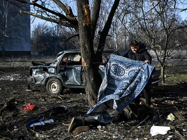 A man uses a carpet to cover a body stretched out on the ground after bombings on the eastern Ukraine town of Chuguiv. Picture: AFP