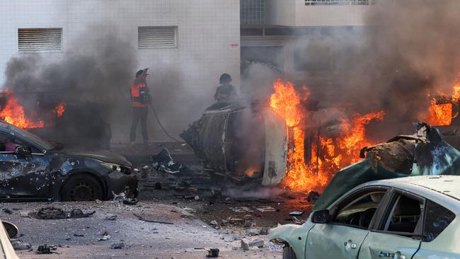 People try to extinguish fire on cars following a rocket attack from the Gaza Strip in Ashkelon, southern Israel, on October 7, 2023. Picture: AFP