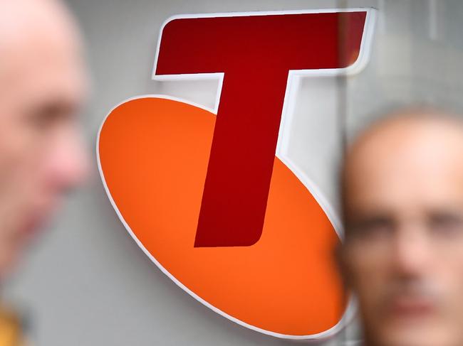 People walk past a sign of telecommunications company Telstra in Melbourne on August 16, 2018. - Australia's dominant telecommunications company Telstra on August 16 warned of 