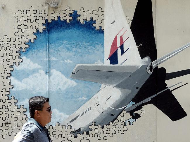 (FILES) This file photo taken on March 8, 2016 shows a Malaysian man walking in front of a mural of missing Malaysia Airlines MH370 plane in a back-alley in Shah Alam. The disappearance of the Boeing 777 carrying 239 passengers and crew almost four years ago is one of aviation's greatest mysteries, with an Australian-led hunt across a 120,000 square-kilometre (46,000 square-mile) zone failing to reveal the crash site.  / AFP PHOTO / Manan VATSYAYANA / TO GO WITH Australia-Malaysia-China-aviation-MH370,FOCUS by Glenda Kwek