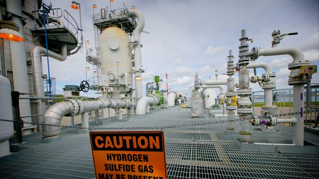 A sign warning of the presence of hydrogen sulfide gas hangs across a walkway at the Queensland Curtis Liquefied Natural Gas (QCLNG) project site, operated by QGC Pty, a unit of Royal Dutch Shell Plc, in Gladstone, Australia. (Photographer: Patrick Hamilton/Bloomberg)