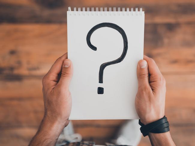 Top view of man holding note pad with question mark on it while standing on the wooden floor