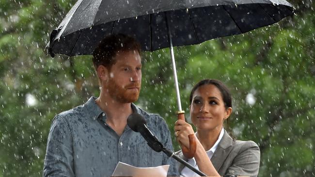 Britain's Prince Harry speaks to the community as his wife Meghan, Duchess of Sussex holds an umbrella under heavy rain in Australia's outback town of Dubbo on October 17, 2018. - The rain was a welcomed accompaniment when Harry and his expectant wife Meghan visited a drought-stricken region of Australia on October 17, where the prince commended resilient farmers for persisting through years-long dry spells. (Photo by PETER PARKS / Pool / AFP)