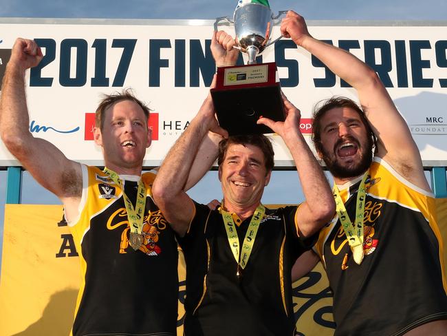 YCW coach Wayne Capp and co captains Jie Coghlan and Ken Lylak hold up the Premiership Cup during the Peninsula League Grand Final between Frankston YCW and Bonbeach played at Kars Park in Frankston on Sunday 17th September, 2017. Picture: Mark Dadswell