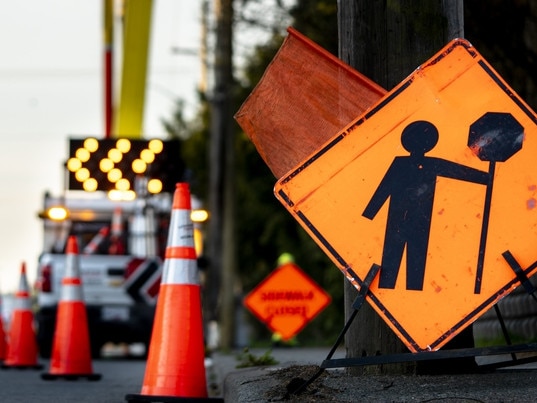 Lane closure on a busy road due to maintenance signs detour traffic temporary street work orange lighted arrow, barrels, and cones. Photo: iStock