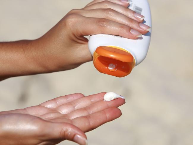 Hands using bottle of sunscreen lotion.