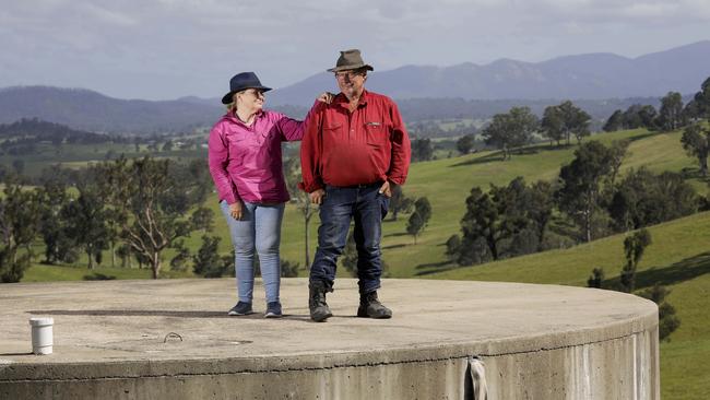 Robyn and Graeme Freedman stand atop their empty 100,000-litre water tank on what’s left of their bushfire-ravaged property in Wandella in southern NSW. Picture: Sean Davey