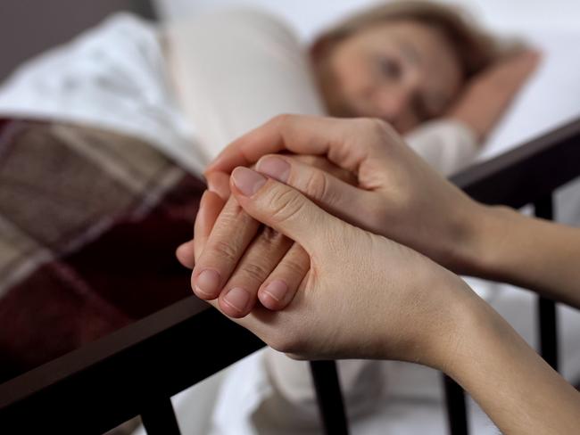 Daughter supporting her terminally ill mother lying on hospital bed, hospice istock image