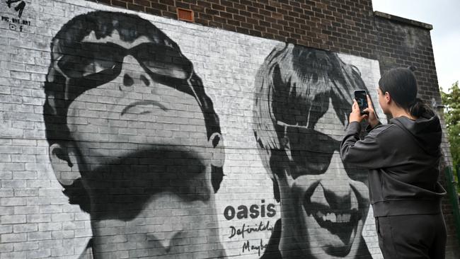 Fan Emily McShane, takes a photograph of a new street artwork depicting Oasis' Liam and Noel Gallagher, created by Manchester-based street artist Pic.One.Art., on the side of the Sifters Record store in Burnage, Manchester. Picture: AFP