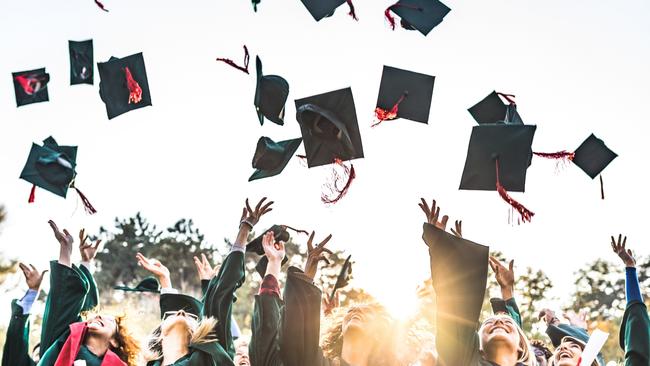 Generic stock photo showing a large group of happy college students celebrating their graduation day outdoors while throwing their caps up in the air.