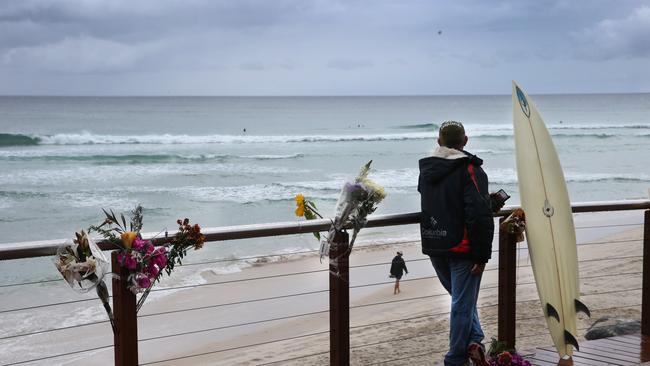 Surfers back in the line up at Greenmount Beach on Thursday as a surfer looks out next to tributes left to Nick Slater, the man who was killed by a great white shark. Picture Glenn Hampson