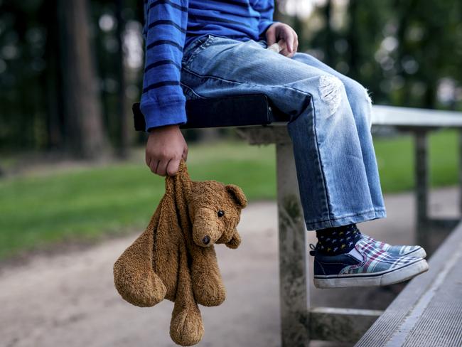 Young boy holding teddybear while alone on the bleachers