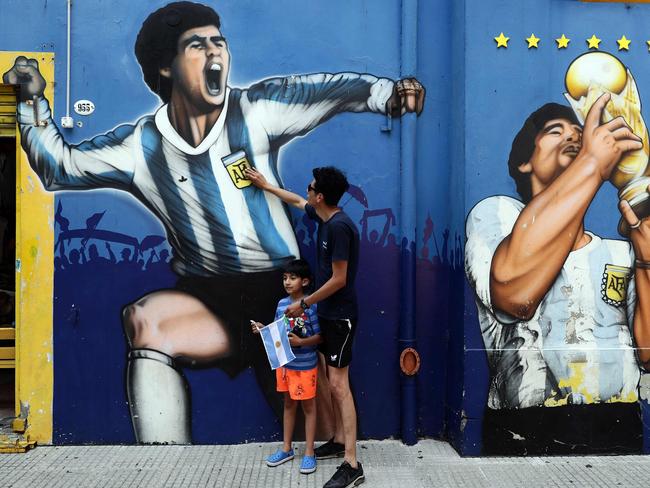 A man and his child pay tribute next to a mural of Diego Maradona in Buenos Aires