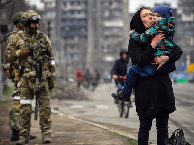 A woman holds and kisses a child next to Russian soldiers in a street of Mariupol. Picture: AFP