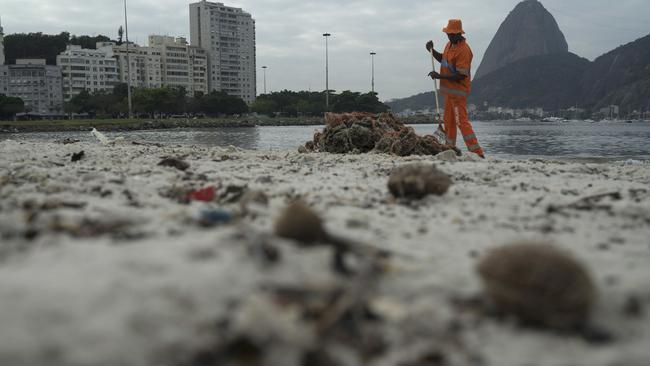 Workers remove trash over the sand of Botafogo beach next to the Sugar Loaf mountain and the Guanabara Bay in Rio de Janeiro.