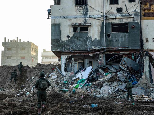 --PHOTO TAKEN DURING A CONTROLLED TOUR AND SUBSEQUENTLY EDITED UNDER THE SUPERVISION OF THE ISRAELI MILITARY-- This picture taken on December 19, 2023, shows Israeli soldiers walking past a damaged building during a military operation in the north of the Gaza Strip amid continuing battles between Israel and the Palestinian militant group Hamas. (Photo by GIL COHEN-MAGEN / AFP)