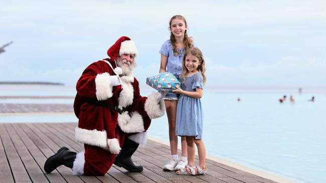 Bruce Skilbeck has been donning the red suit as Santa Claus at DFO Shopping Centre this year, spreading the joy of the Christmas season to the young and the young at heart. Santa, aka Bruce Skilbeck, gifts a Christmas present to his granddaughters Lilly Hogan, 11, and Grace Hogan, 5, at the Esplanade Lagoon. Picture: Brendan Radke