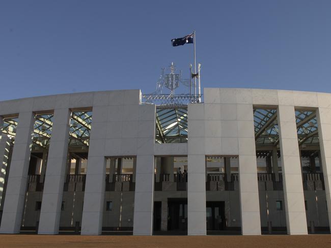 The Australian Coat of Arms that includes and kangaroo and emu above the front entrance of Parliament House in Canberra with the giant Australian flag flying on the top of the building behind.