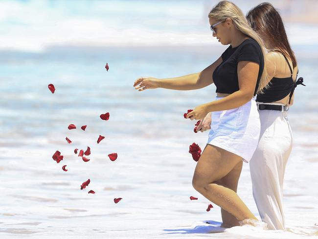 Chris Caserta’s partner Brittany Wise sprinkles rose petals in the surf where he drowned last week. Picture: Adam Head