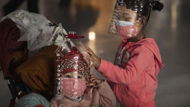 Chinese children wear plastic bottles as makeshift homemade protection and protective masks while waiting to check in to a flight at Beijing Capital Airport in Beijing. Picture: Kevin Frayer/Getty