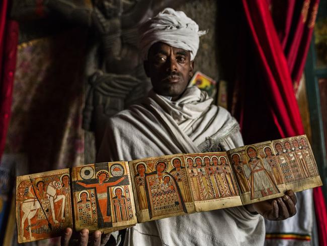 A priest holds a manuscript depicting Jesus and St George, among other religious figures. Picture: Tariq Zaidi / Caters News