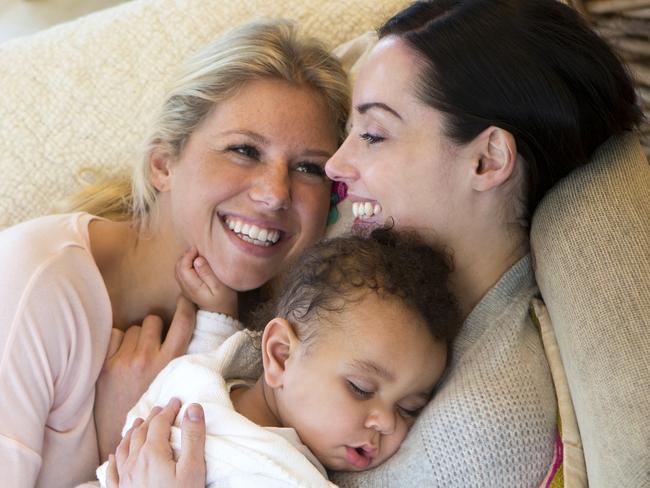 Same sex female couple cuddling on the sofa with their sleeping son