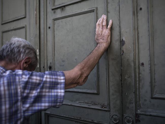 Citizens fearing the worst ... A pensioner leans against the gate of the National Bank of Greece as he waits to withdraw money. Picture: AFP/ANGELOS TZORTZINIS