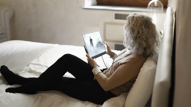 Mature businesswoman sitting on bed looking at digital tablet