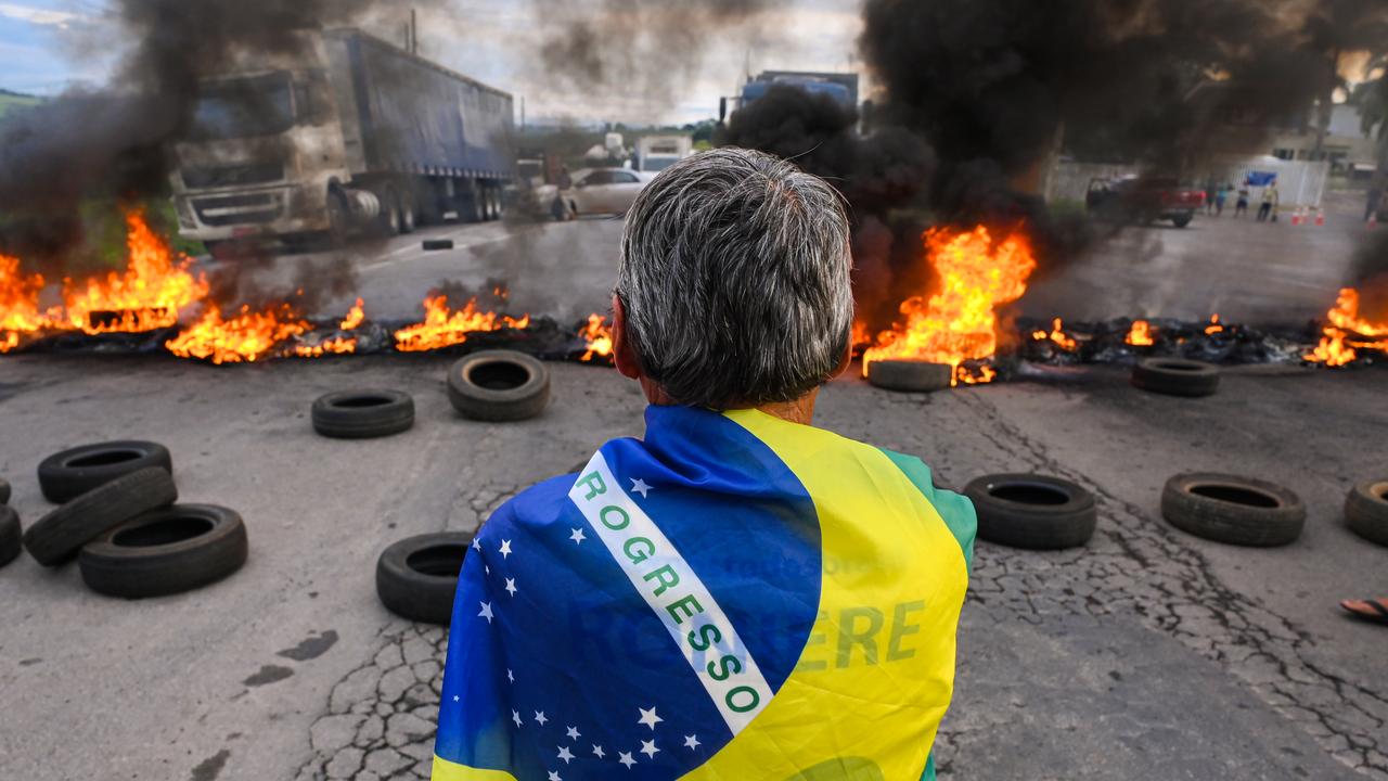 Um manifestante usando uma bandeira brasileira fica enquanto caminhoneiros e apoiadores do presidente Jair Bolsonaro bloqueiam a estrada com barricadas em chamas para protestar contra os resultados do segundo turno presidencial.  (Foto de Pedro Vilela/Getty Images)