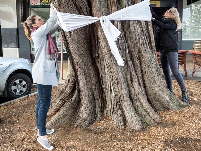 Women tie a white ribbon to a tree to honour Samantha Fraser. Picture: Jake Nowakowski