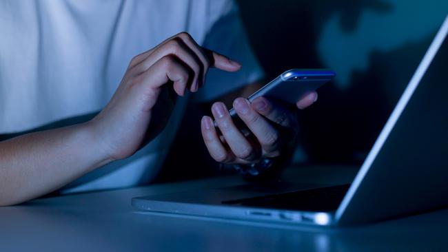 Close up young man hand holding smartphone for access by unlock on screen and using laptop for register website on internet in the late night, internet addiction concept.