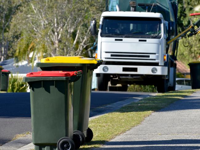 Focus on two Rubbish bins with rubbish truck in background lifting a bin