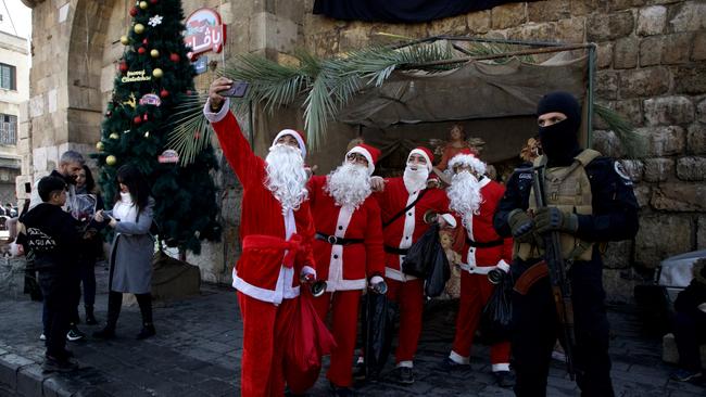 People dressed as Santa Claus pose for a selfie while a man holding a weapon stands guard in Damascus, Syria. Picture: Getty Images